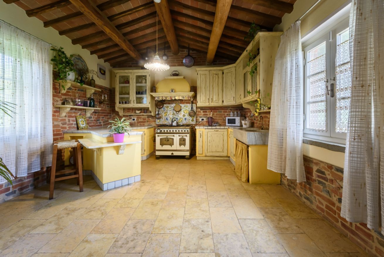 Een keuken met zichtbare bakstenen muren, houten balken, een geel kookeiland en een retro fornuis.