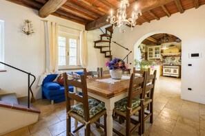 A dining area with a wooden table, chairs, and a chandelier. A staircase leads to a second floor.