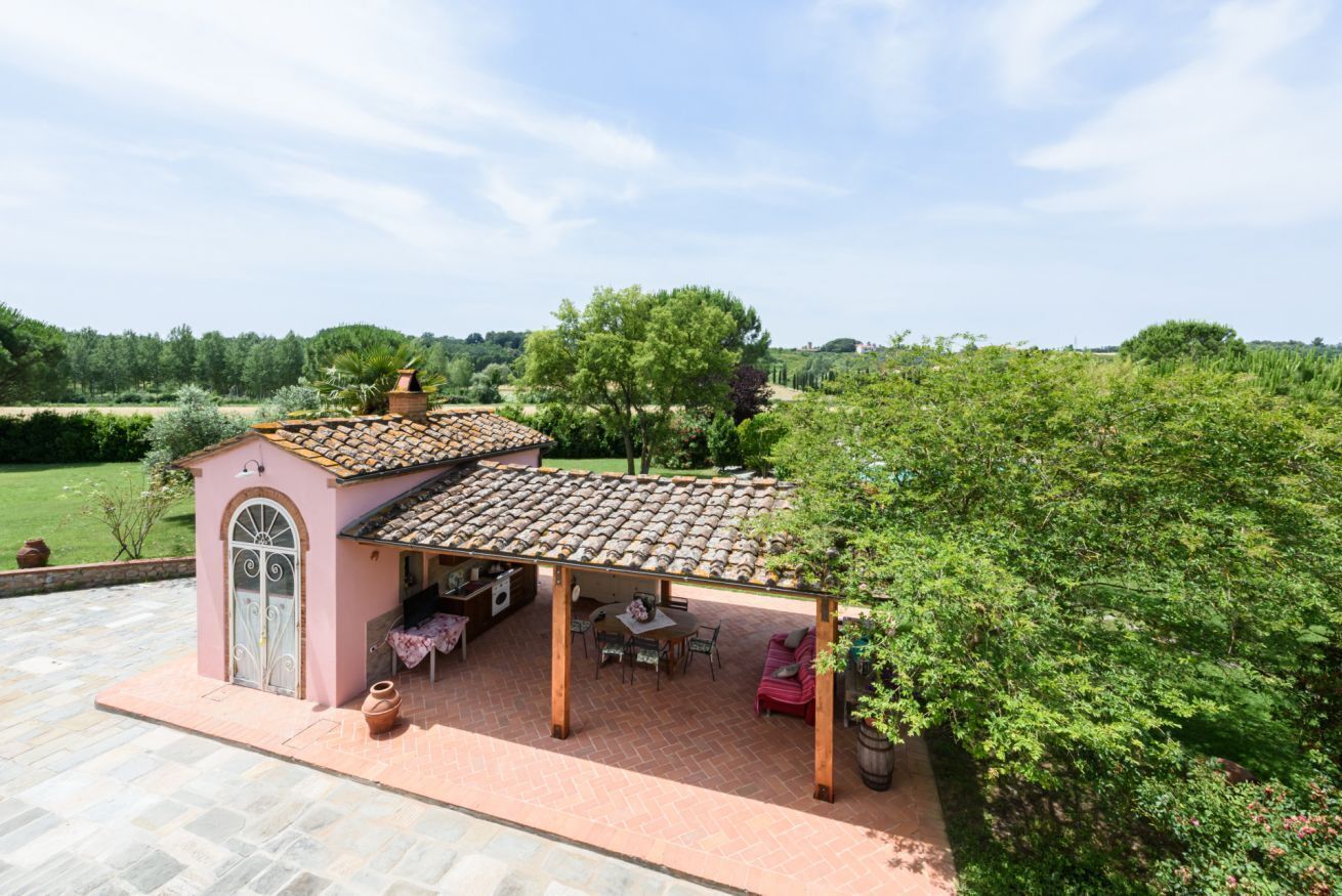 A small house with a tiled roof, a patio with outdoor furniture, and a view of the surrounding greenery.