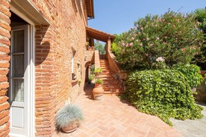 A brick building with a covered outdoor area, steps leading to a door, and potted plants. - Villa al Molino By MMega (Fauglia)