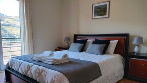 A hotel room with a large bed, two bedside tables with lamps, a view of the countryside through the window, and a framed picture on the wall.