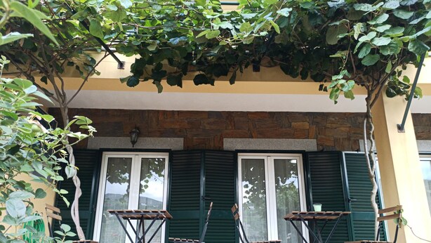 A patio area with a stone wall, green shutters, and two folding tables with chairs.