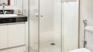 Un baño moderno con ducha de vidrio, inodoro blanco y encimera de mármol con lavamanos.