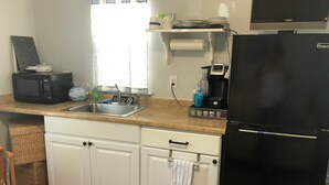 Une cuisine de taille réduite avec des meubles blancs, un réfrigérateur noir, un four à micro-ondes, une machine à café et un évier.