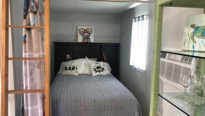 Une chambre à coucher comprenant un lit, une tête de lit, une fenêtre, une étagère avec des objets décoratifs et une porte avec des rideaux.