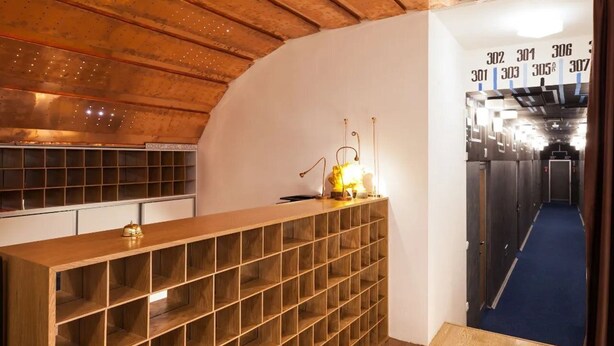 A hotel corridor with a wooden ceiling, a reception desk with a light, and a blue carpet. - Concept Hotel Central (Skopje)