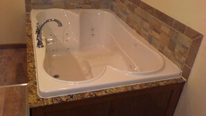 A rectangular bathtub with a chrome faucet, set against a stone tile backsplash. - Condos.  hot tub, deck,  Patoka lake (8800 acres) boating and beach, concessions   (French Lick)