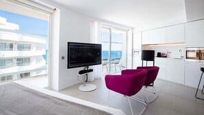 Ein modernes Hotelzimmer mit großem Fernseher, einem Balkon mit Meerblick und einer Küchenzeile.
