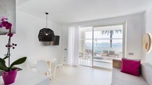 Ein modernes Wohnzimmer mit Balkon und Meerblick, mit weißer Möbel und einer Topforchidee.