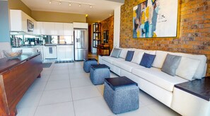 Ein modernes Wohnzimmer mit einem weißen Sofa, grauen Poufs und einem Holztisch.
