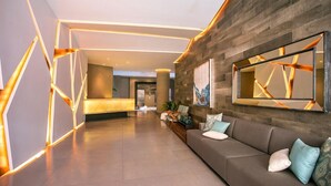 A modern lobby with a reception desk, a sofa with cushions, and a large mirror reflecting the interior.