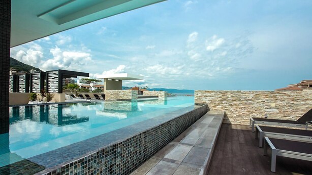 A modern infinity pool with a clear view of the sea, surrounded by stone walls and lounge chairs.