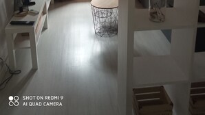 Een kamer met een wit bureau, twee ronde tafels, een klein plankje met decoratieve objecten, en een raam met gordijnen.