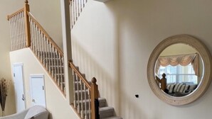 Un salon avec un tapis beige, un escalier en bois, un miroir rond et un canapé.