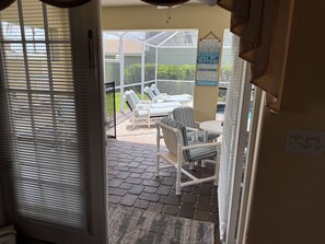 Vue depuis l’intérieur d’une pièce sur un patio extérieur avec une table, des chaises et un panneau indiquant les règles à respecter.
