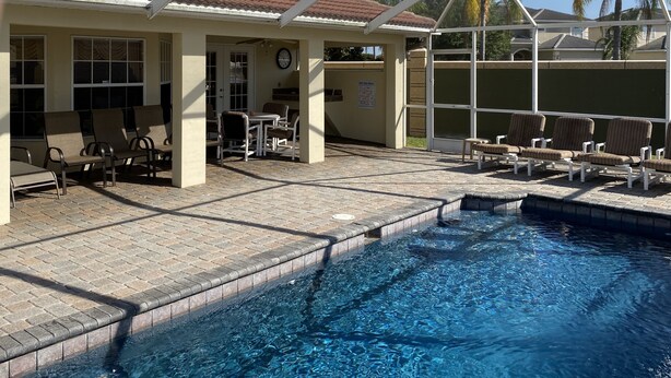 Un espace piscine extérieur abrité, doté de chaises longues et d’une table, entouré d’une maison avec un toit en tuiles et des fenêtres.