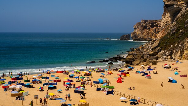 A beach with numerous umbrellas and tents, rocky cliffs, and a clear blue sky. - Peace & Love Flat Nazaré - Peace & Love (Nazaré)