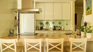 A modern kitchen with a central island, white cabinetry, and a backsplash with decorative tiles. - Peace & Love Flat Nazaré - Peace & Love (Nazaré)