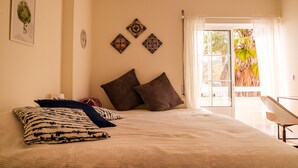 A neatly made bed with patterned pillows, a wall with decorative tiles, and a view of palm trees through a window. - Peace & Love Flat Nazaré - Peace & Love (Nazaré)