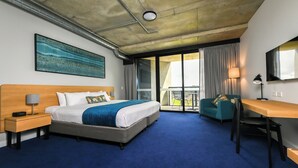 Habitación de hotel con cama, escritorio, silla, mesita de noche, lámpara y ventana grande.