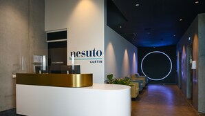 Un mostrador de recepción de diseño moderno, un cartel que dice "nesuto curtin" y un pasillo con asientos y un elemento de iluminación circular.