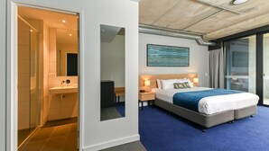 Habitación de hotel moderna con una cama grande, un baño con cabina de ducha de vidrio y vistas a través de un ventanal corredera.