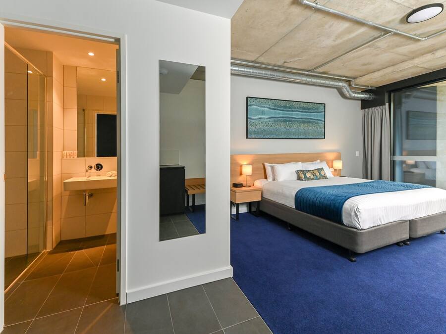 Habitación de hotel moderna con una cama grande, un baño con cabina de ducha de vidrio y vistas a través de un ventanal corredera.