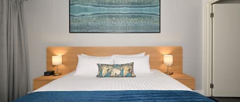 Een hotelkamer met een groot bed, twee bedlampen, een hoofdeinde, een kunstwerk aan de muur en een deur.
