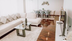 Uma sala de estar moderna com um sofá, uma mesa de centro de vidro e uma área de jantar com mesa e cadeiras.