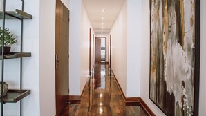 Um corredor com piso de madeira, uma grande pintura abstrata à direita e uma estante de metal à esquerda.