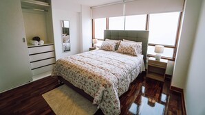 Quarto com cama grande, mesa de cabeceira, guarda-roupa e janela com persianas.