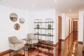 A modern living room with two armchairs, a small table, and a decorative shelf with plants and vases.