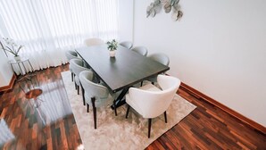 Uma área de refeições com uma mesa retangular, seis cadeiras, um tapete branco e um objeto decorativo fixado na parede.