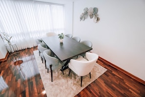 Uma área de refeições com uma mesa retangular, seis cadeiras, um tapete branco e um objeto decorativo fixado na parede.