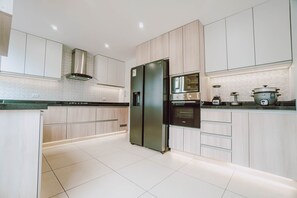 A modern kitchen with light wood cabinets, stainless steel appliances, and a tiled floor.