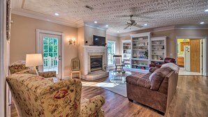 A living room with a fireplace, floral armchairs, a brown sofa, and a glass coffee table. - Luxe Lake Cumberland Retreat w/ Decks on 1 Acre! (Jamestown)