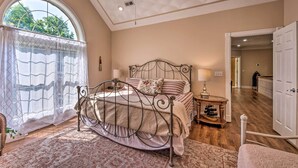 A bedroom with a large bed, a bedside table with a lamp, and a view through a window with curtains. - Luxe Lake Cumberland Retreat w/ Decks on 1 Acre! (Jamestown)