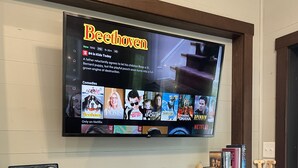 Litteänäyttöinen televisio on kiinnitetty puiseen seinään takan yläpuolelle, ja sen läheisyydessä on kirjoja sekä koriste-esineitä.