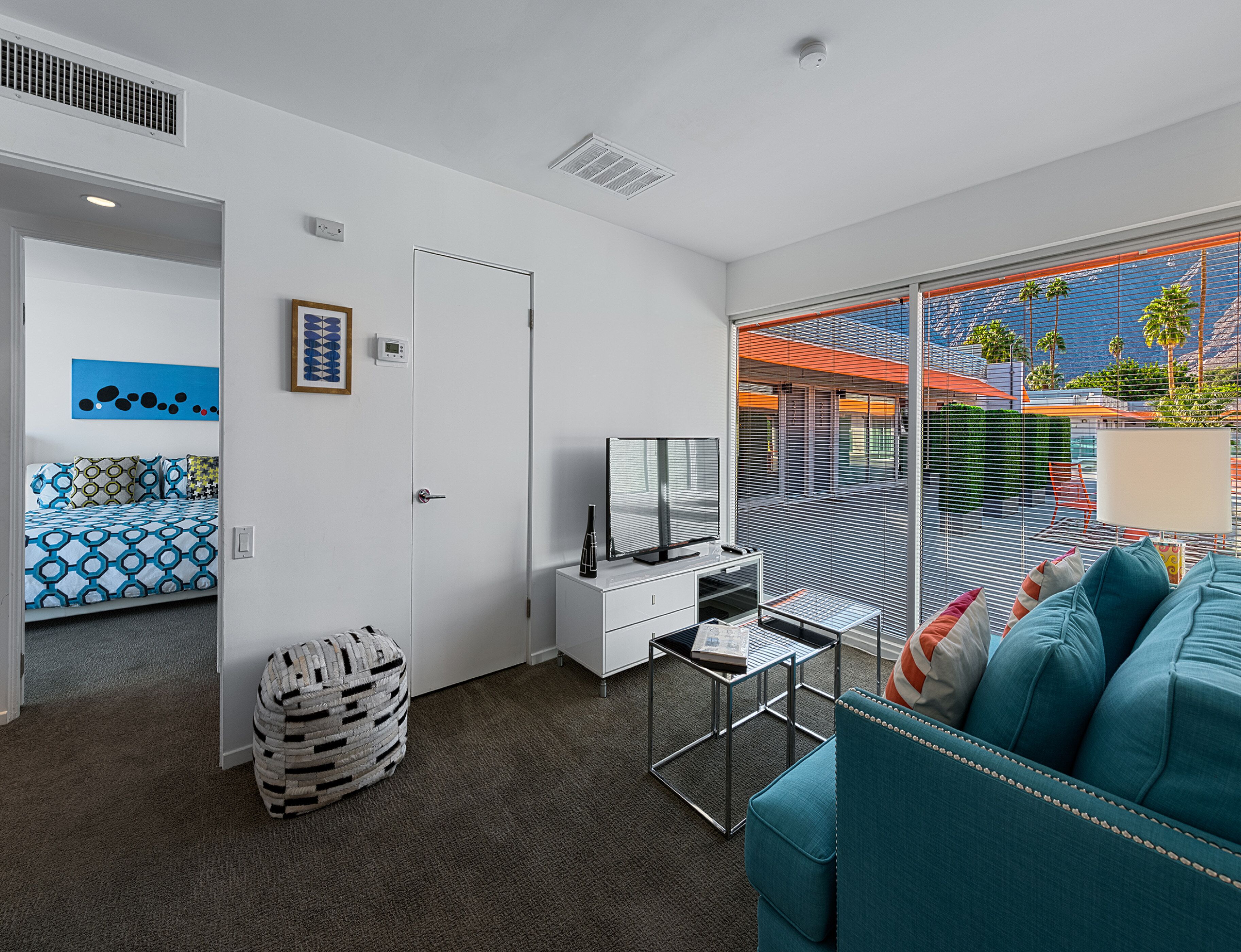 A modern living room with a sofa, a TV, a desk, and a large window with blinds.