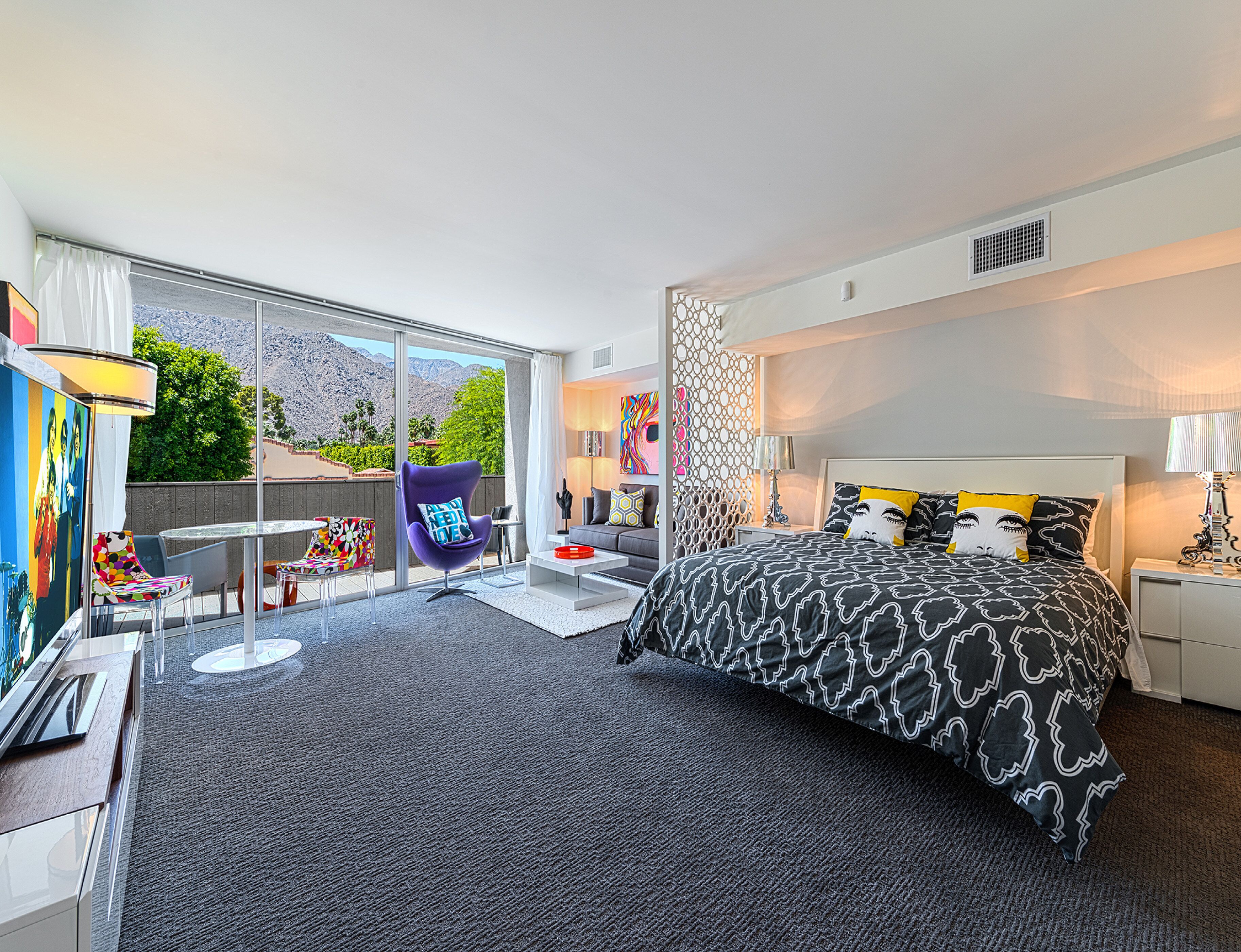 A modern hotel room with a large bed, a seating area with a chair and table, and a view of the outdoors.