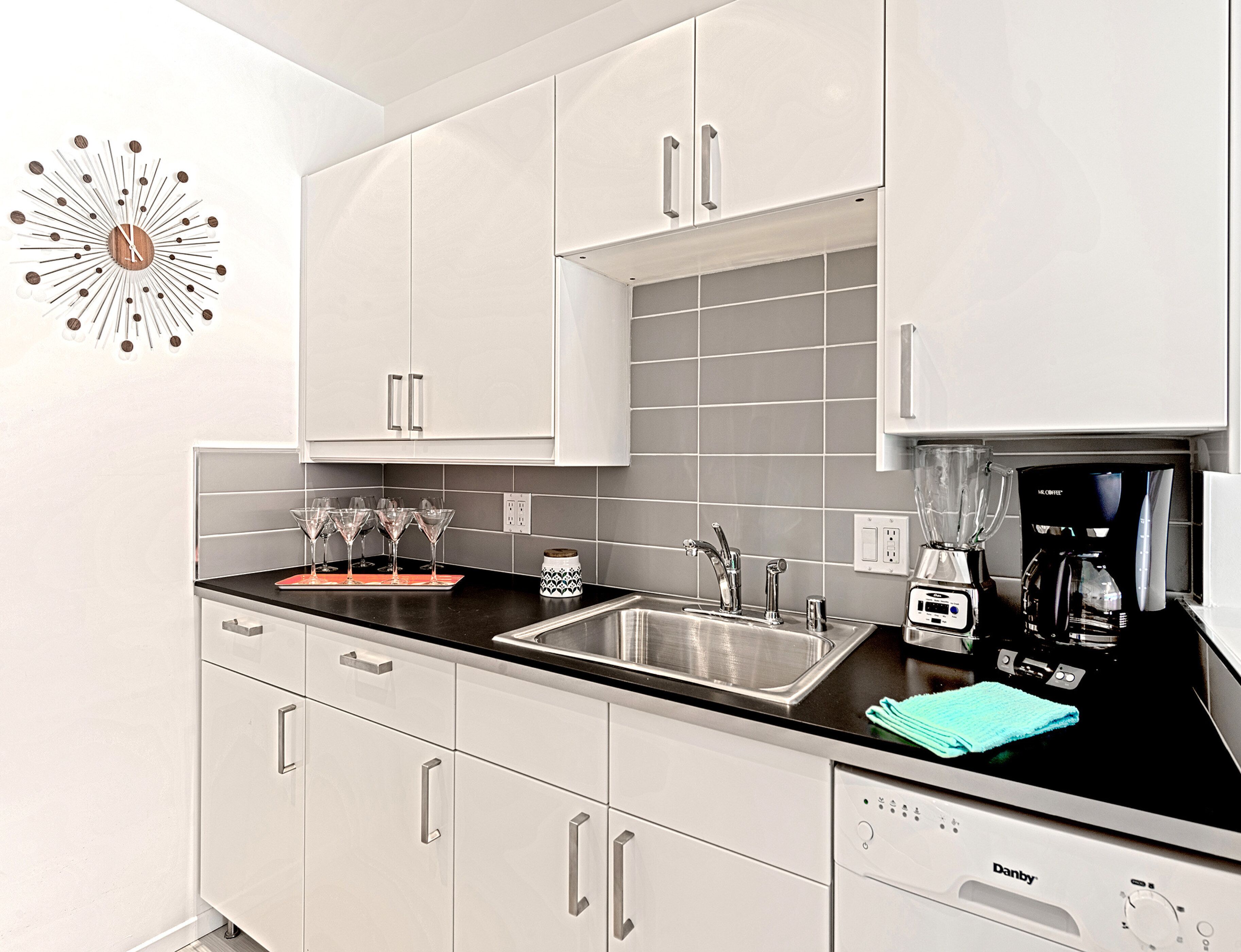 A modern kitchen with white cabinets, a black countertop, a coffee maker, and a blender.