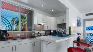 A modern kitchen with white cabinets, a central island, and a dining area with red chairs.
