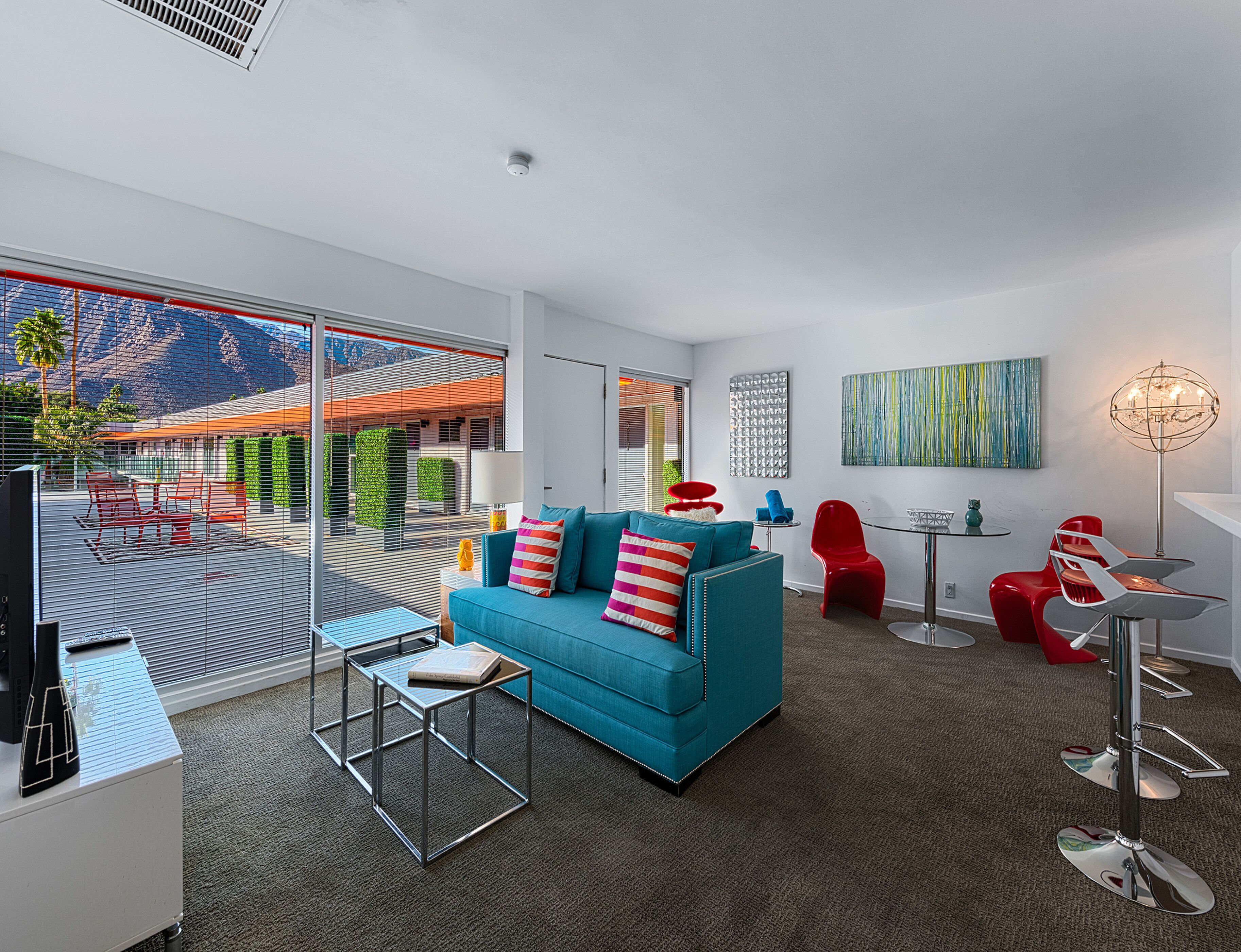 A modern living room with a blue sofa, red chairs, a glass coffee table, and a view of a mountain through large windows.