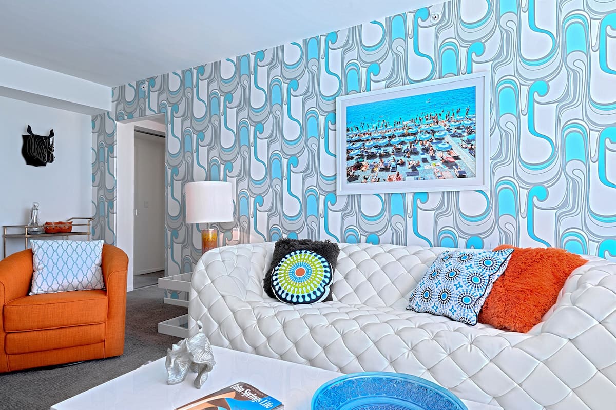 A modern living room with a white sofa, orange armchair, and a coffee table with a magazine and a blue bowl.