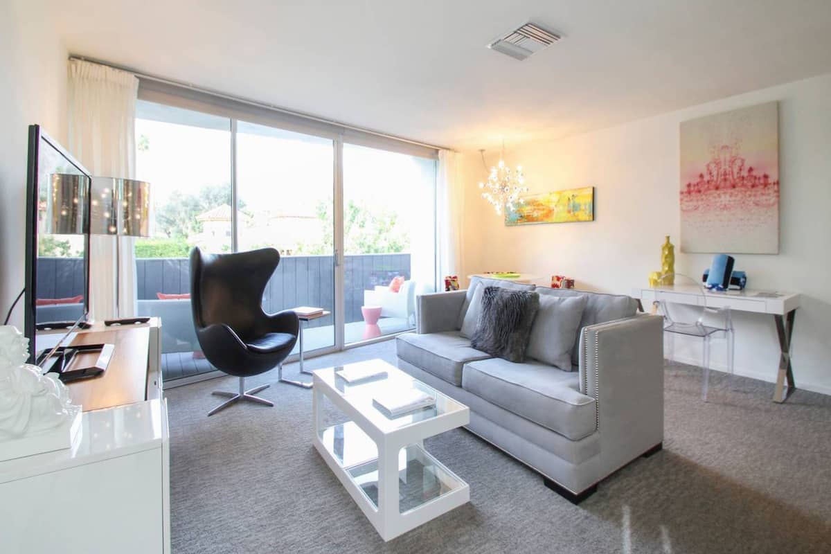 A modern living room with a grey sofa, a black chair, a white coffee table, and a desk with a computer.
