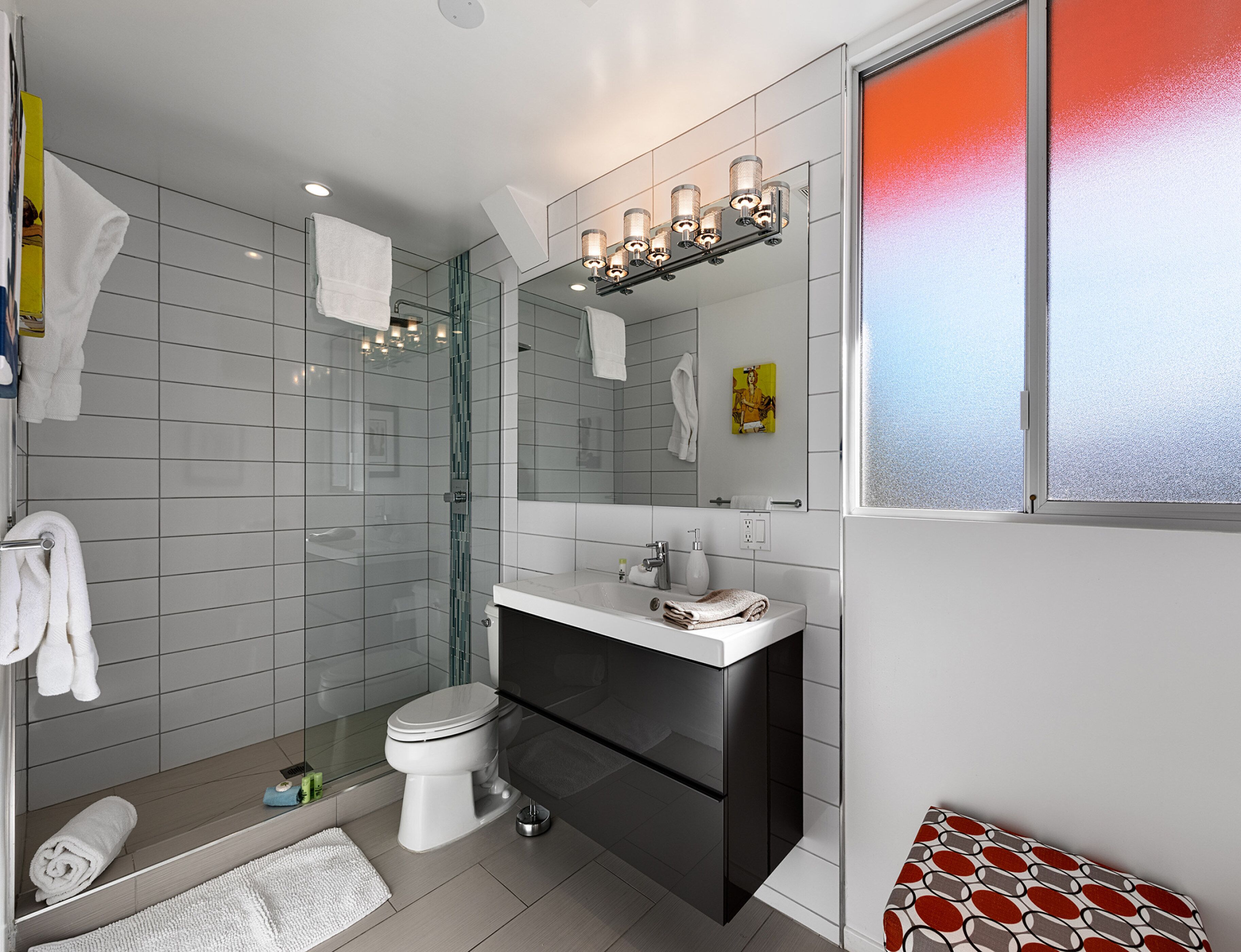 A modern bathroom with a glass shower enclosure, a white toilet, a black vanity, and a large mirror.
