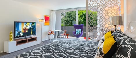 A modern bedroom with a large bed, a television, and a view of greenery outside.