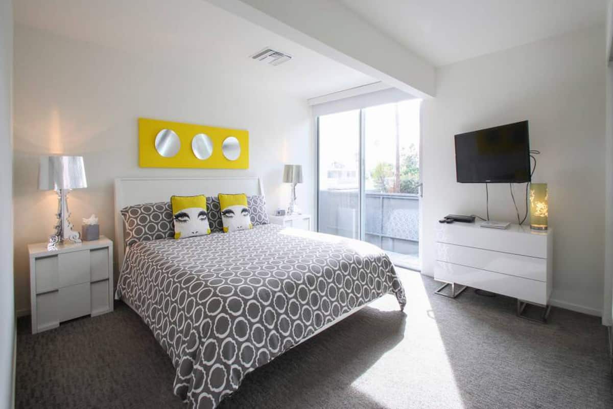 A modern hotel room with a large bed, a flat-screen TV, a white dresser, and a balcony with a view.