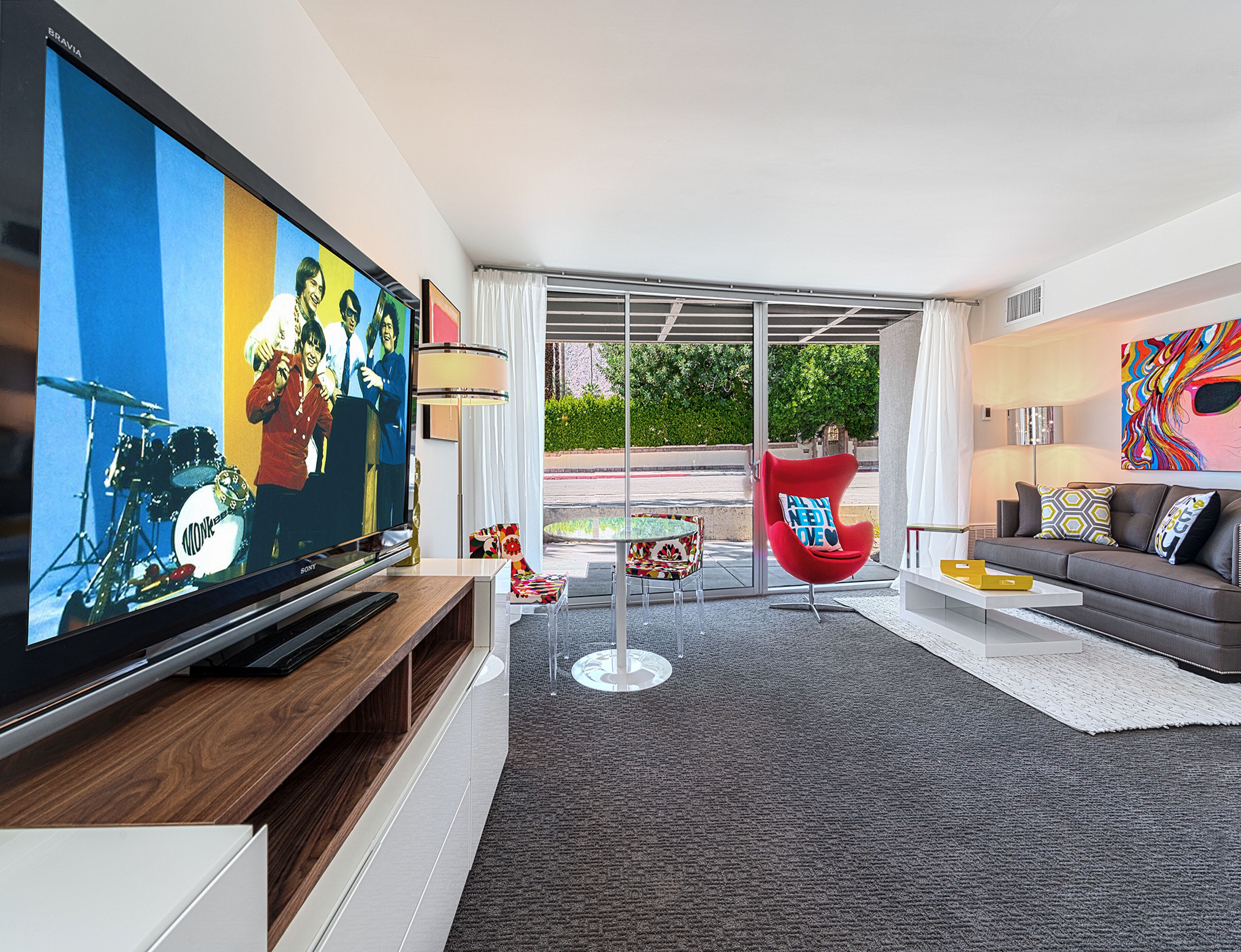 A modern living room with a flat-screen TV, a red chair, a grey sofa, and a colorful painting.