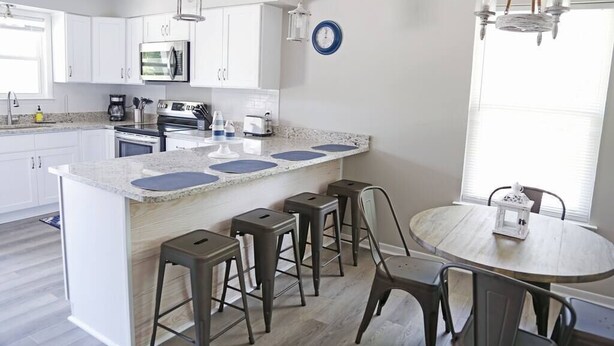 Cocina moderna con armarios blancos, encimera de granito y taburetes de bar.